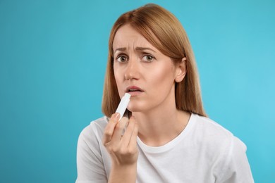 Upset woman with herpes applying lip balm against light blue background