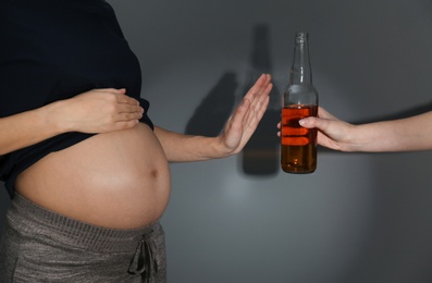 Pregnant woman declining whiskey on dark background. Alcohol harm