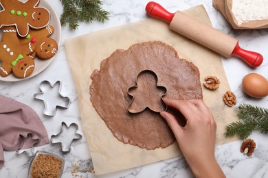Photo of Woman making Christmas gingerbread man cookies at white marble table, top view