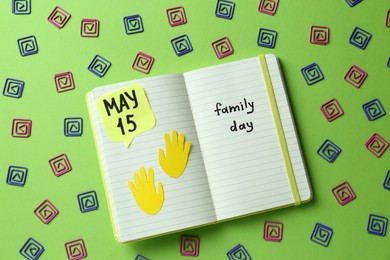 Happy Family Day. Notebook with text and decorative paper clips on light green background, flat lay