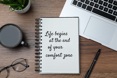 Life Begins At The End Of Your Comfort Zone. Motivational quote inspiring to do something new, different from ordinary life. Text in notebook, laptop, cup of coffee, eyeglasses and houseplant on wooden table, flat lay