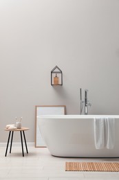 Modern ceramic bathtub near light wall indoors
