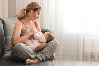Young woman breastfeeding her baby at home. Space for text