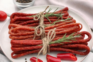 Photo of Bundles of delicious kabanosy with rosemary and chilli on white wooden table, closeup