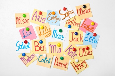 Photo of Colorful paper sheets with written different baby names on white background, flat lay