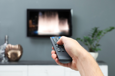 Man switching channels on TV set with remote control at home