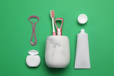 Flat lay composition with tongue cleaners and teeth care products on green background