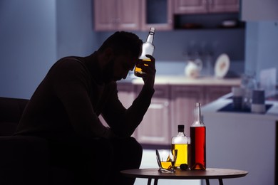 Silhouette of addicted man with alcoholic drinks in kitchen