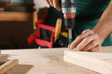 Professional carpenter twisting screw with drill at workbench, closeup. Space for text