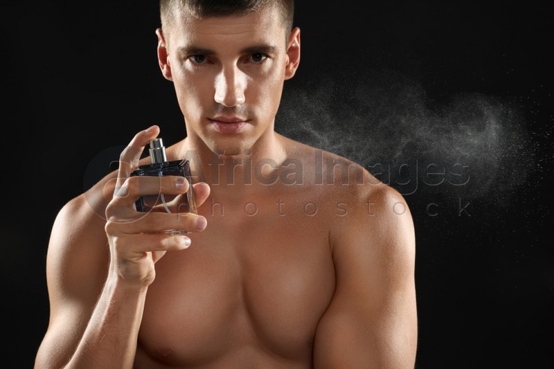Handsome young man spraying perfume on black background