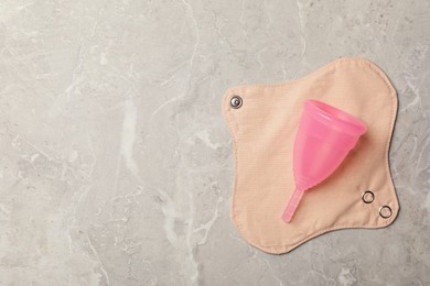 Menstrual cup and cloth pad on grey background, top view. Space for text