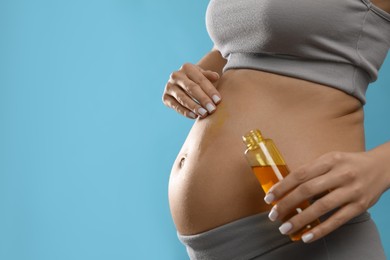 Pregnant woman applying cosmetic product on belly against light blue background, closeup. Space for text
