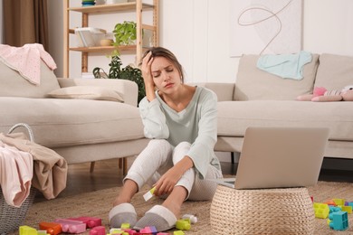 Tired young mother sitting on floor in messy living room