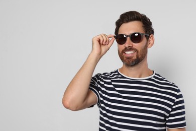 Portrait of smiling bearded man with stylish sunglasses on light grey background. Space for text