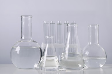 Photo of Different laboratory glassware with transparent liquid on table against light background