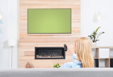 Photo of Woman watching TV on sofa in living room with decorative fireplace