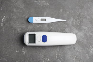 Non-contact infrared and digital thermometers on grey stone background, flat lay