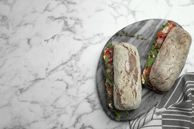 Photo of Delicious sandwiches with fresh vegetables and prosciutto on white marble table, top view. Space for text
