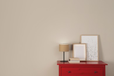 Red chest of drawers with lamp, books, picture and photo frame near light wall, space for text. Interior design
