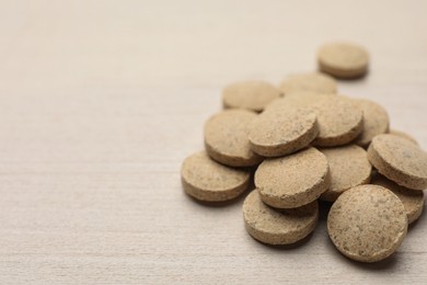 Photo of Dietary supplement pills on white wooden table, closeup. Space for text