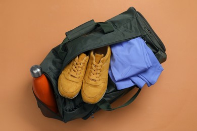 Sports bag with sneakers, clothes and bottle on pale brown background, top view
