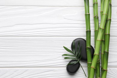 Photo of Spa stones and bamboo stems on white wooden table, flat lay. Space for text