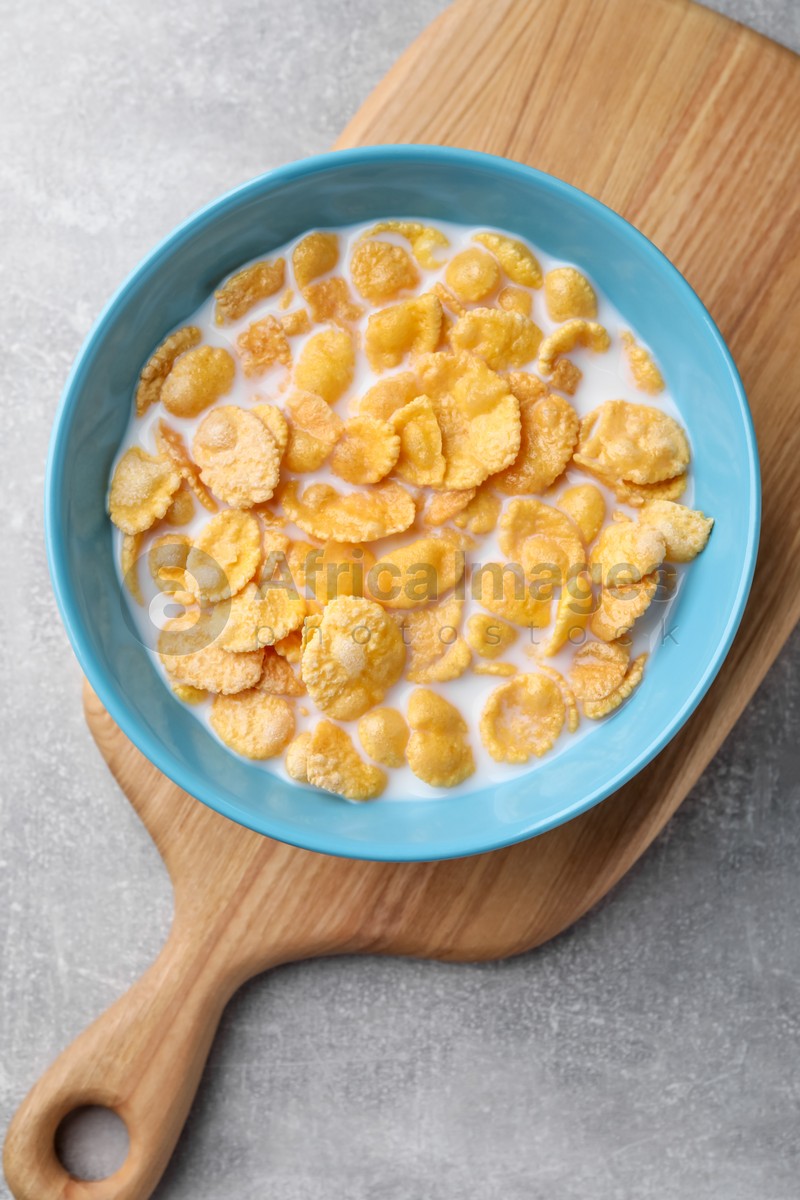 Bowl with tasty cornflakes and milk on light grey table, top view
