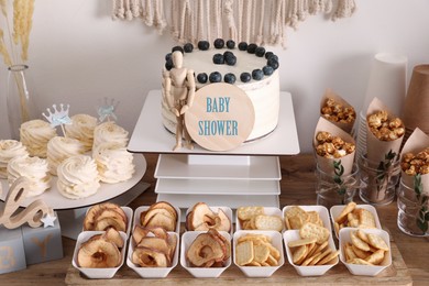 Baby shower party. Different delicious treats and decor on wooden table near light wall