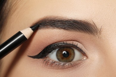 Photo of Young woman correcting eyebrow shape with pencil, closeup view