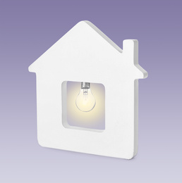 Model of house with glowing light bulb on purple background. Energy efficiency, loan, property or business idea concepts