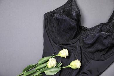 Elegant black plus size women's underwear and beautiful eustoma flowers on grey background, top view. Space for text