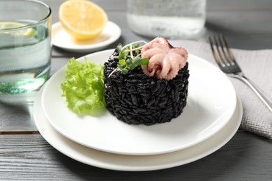 Photo of Delicious black risotto with baby octopus on grey wooden table