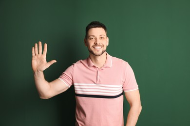 Photo of Cheerful man waving to say hello on green background