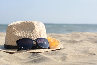 Photo of Hat with beautiful sunglasses and flowers on sand near sea. Space for text