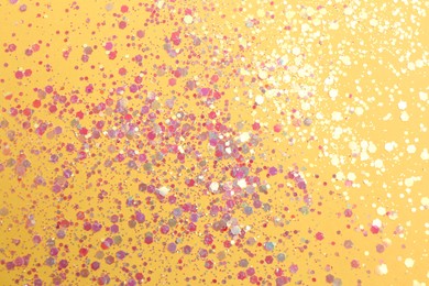 Photo of Shiny bright glitter on yellow background, flat lay