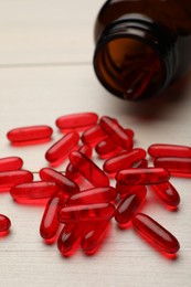 Photo of Overturned bottle with dietary supplement capsules on white wooden table, closeup
