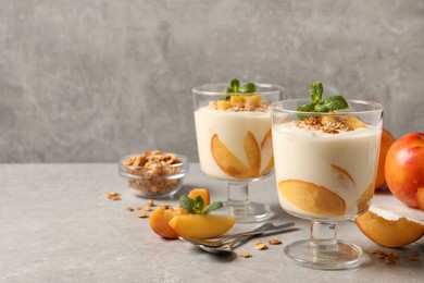 Tasty peach yogurt with granola, mint and pieces of fruits on light grey table, space for text