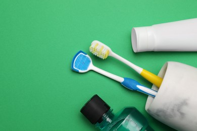 Flat lay composition with tongue cleaner and teeth care products on green background, space for text