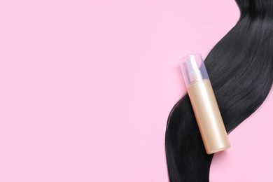 Photo of Spray bottle with thermal protection and lock of black hair on pink background, flat lay. Space for text