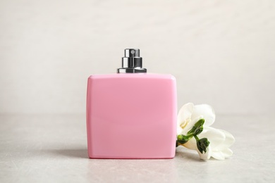 Bottle of perfume and beautiful freesia flower on light table