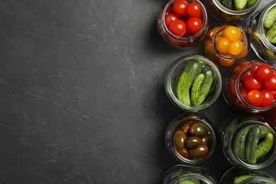 Pickling jars with fresh vegetables on black table, flat lay. Space for text