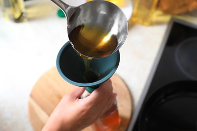 Woman pouring used cooking oil into bottle through funnel in kitchen, closeup