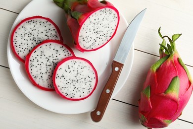 Plate of delicious cut and whole pitahaya fruits with knife on white wooden table, flat lay