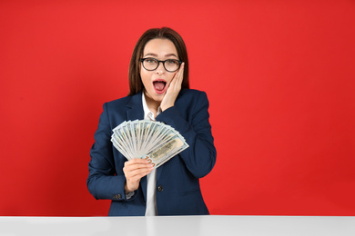 Emotional young woman with money at table on crimson background