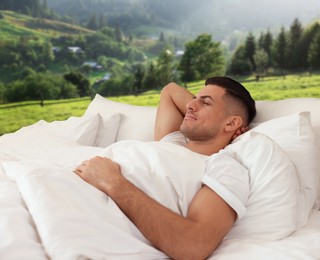 Happy man sleeping in bed and beautiful view of mountain landscape on background. Sleep well - stay healthy