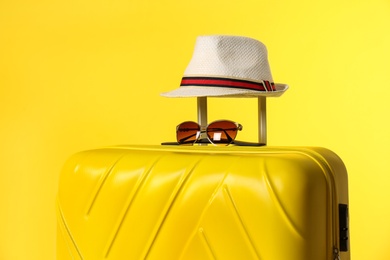 Stylish suitcase with hat and sunglasses on color background