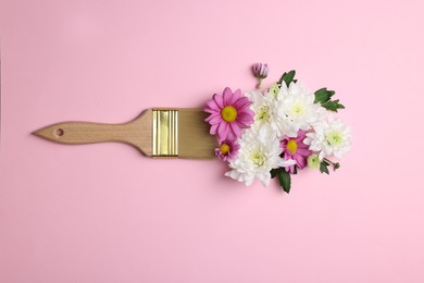 Brush with colorful flowers of chrysanthemum on light pink background, top view. Creative concept