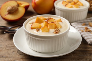Tasty peach yogurt with granola and pieces of fruit in bowl on wooden table