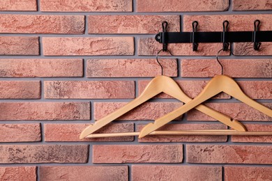 Hook rack with wooden clothes hangers on red brick wall. Space for text