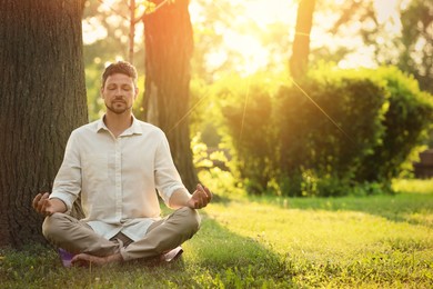 Man meditating in park on sunny morning. Practicing yoga